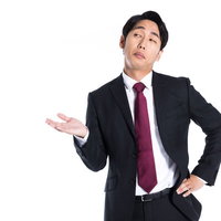 挑発的な態度で片手を広げて案内するスーツ姿の男性の写真