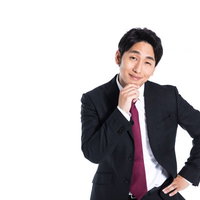 紺色のスーツに赤いネクタイの会社員が浮かべる不敵な笑みの写真