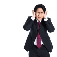 両手で耳をふさいで頭痛に苦悶するスーツの男性の写真
