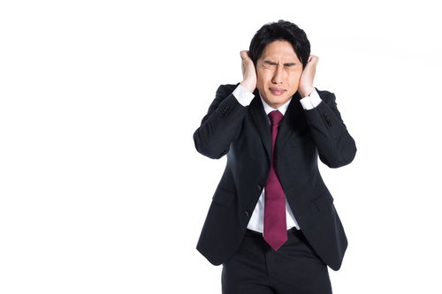 両手で耳をふさいで頭痛に苦悶するスーツの男性