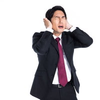 両手で耳を塞いで頭痛に苦しむスーツ姿の男性の写真