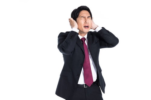 両手で耳を塞いで頭痛に苦しむスーツ姿の男性