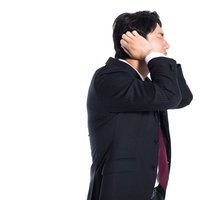 失敗して頭を抱えて耳を塞ぐ困惑したスーツ姿の会社員男性の写真