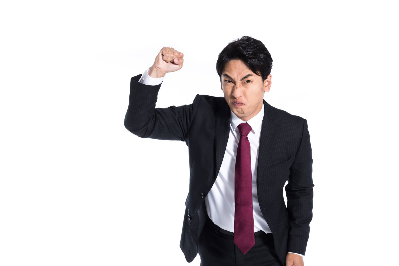 紫紅色のネクタイをした男性が両目を吊り上げ、拳を握ってビジネススーツを着たまま怒りを表現している［モデル：大川竜弥］