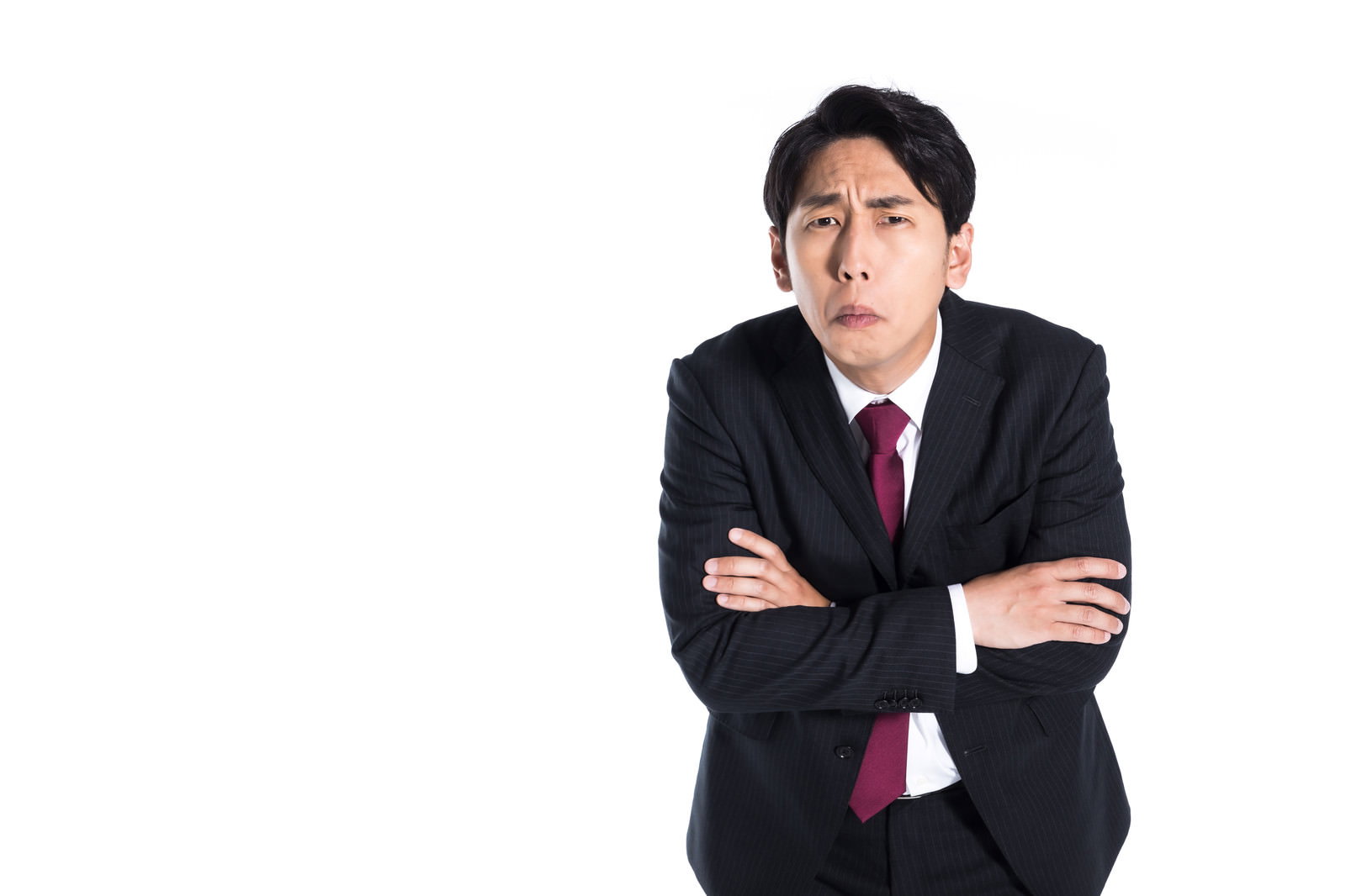 黒いスーツを着て腕組みをし、困った表情を浮かべる会社員の男性［モデル：大川竜弥］