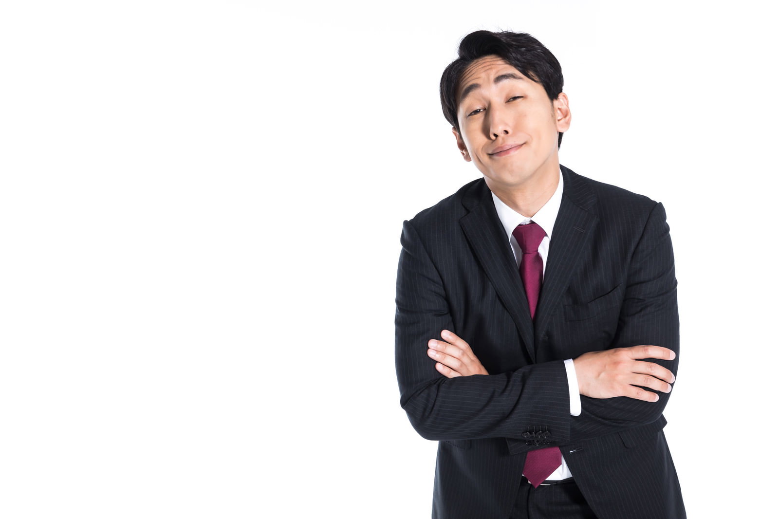 腕を組んで斜め上を見ながら不遜な笑顔を浮かべるスーツの男性［モデル：大川竜弥］