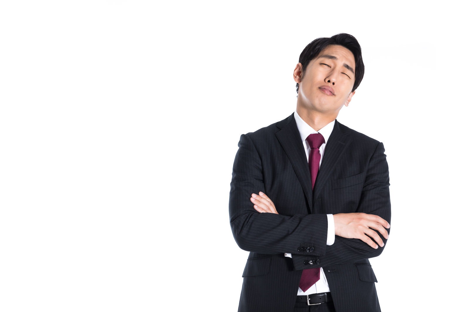 黒いストライプのスーツとエンジ色ネクタイの男性が両腕を組み、目を閉じ顔を上に向け困った表情で立つ［モデル：大川竜弥］