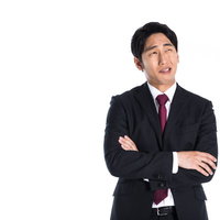 腕を組んで上を見つめ考え込むスーツ男性の写真