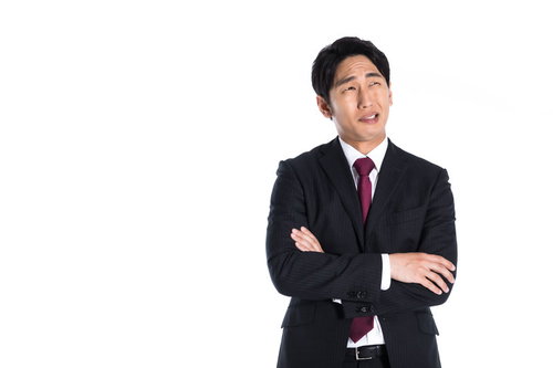 腕を組んで上を見つめ考え込むスーツ男性