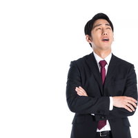 腕を組んで上を向く困った表情のスーツ姿男性の写真