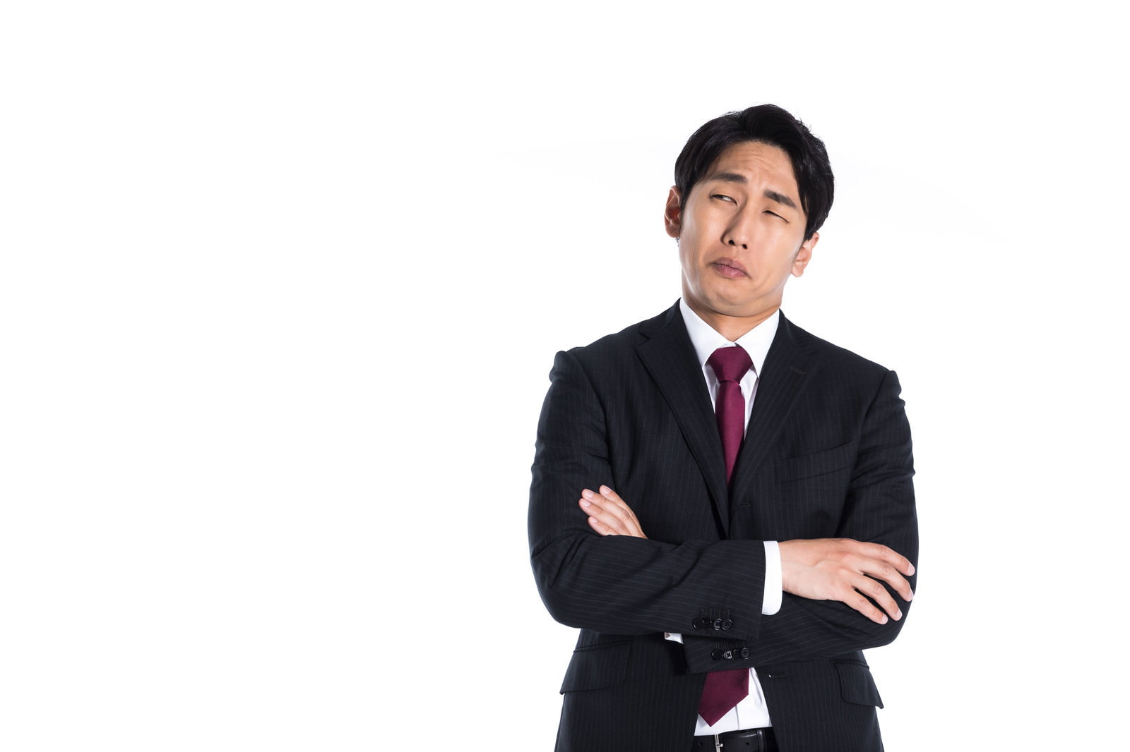両腕を組んで上方を見つめ、眉をひそめて考え込むスーツ姿の男性［モデル：大川竜弥］