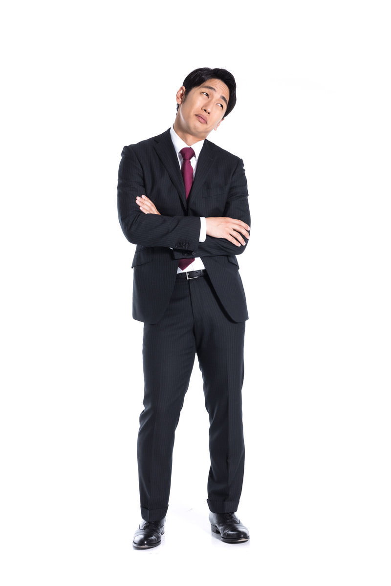 黒いストライプスーツを着た男性が両腕を組み、困った表情で上方を見つめている［モデル：大川竜弥］