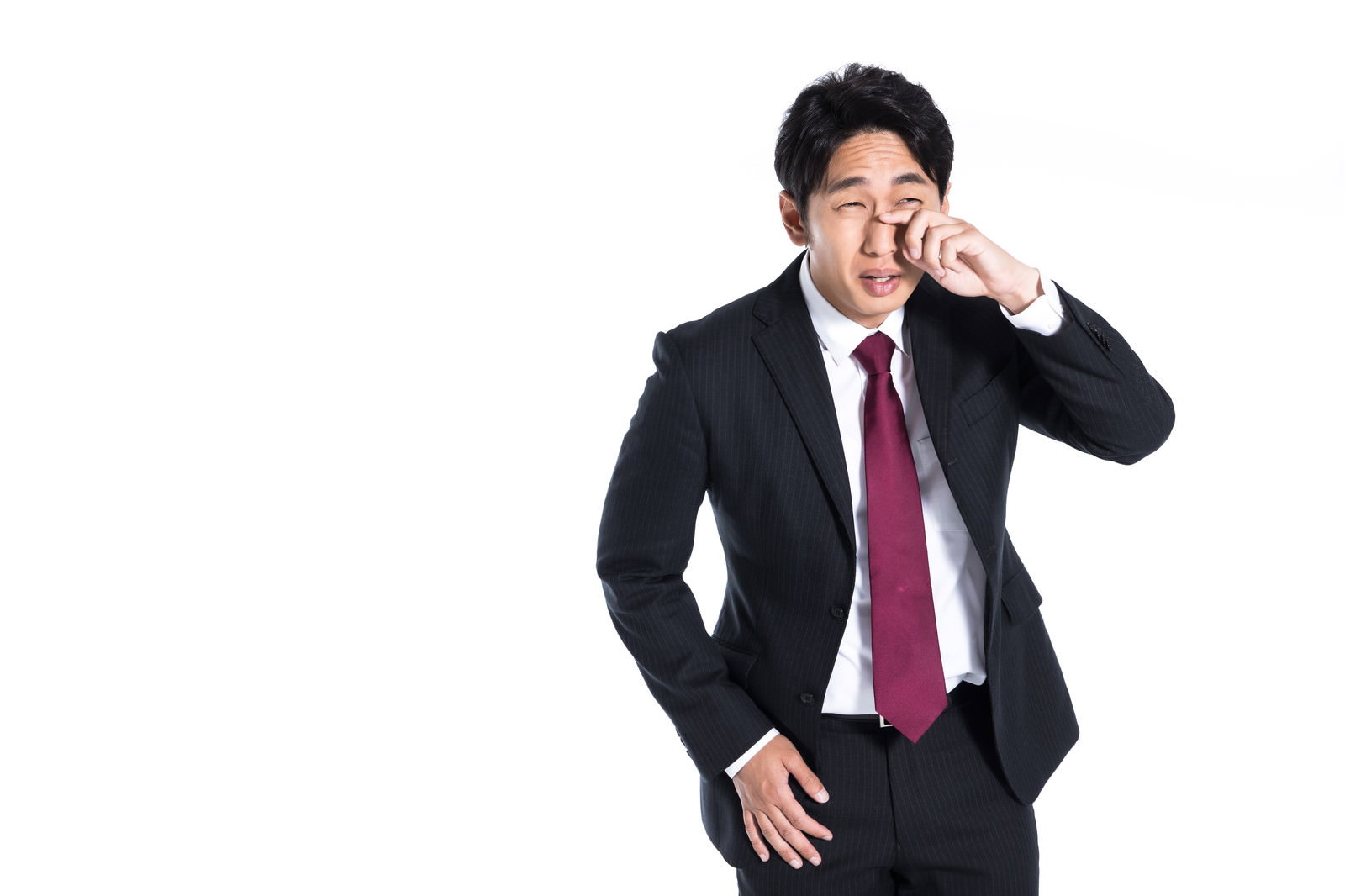 紺色のスーツに赤いネクタイを着た営業マンが右手で目元を押さえて泣いている［モデル：大川竜弥］