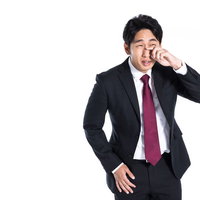 紺色のスーツ姿で後悔と悔しさに泣く営業マンの写真