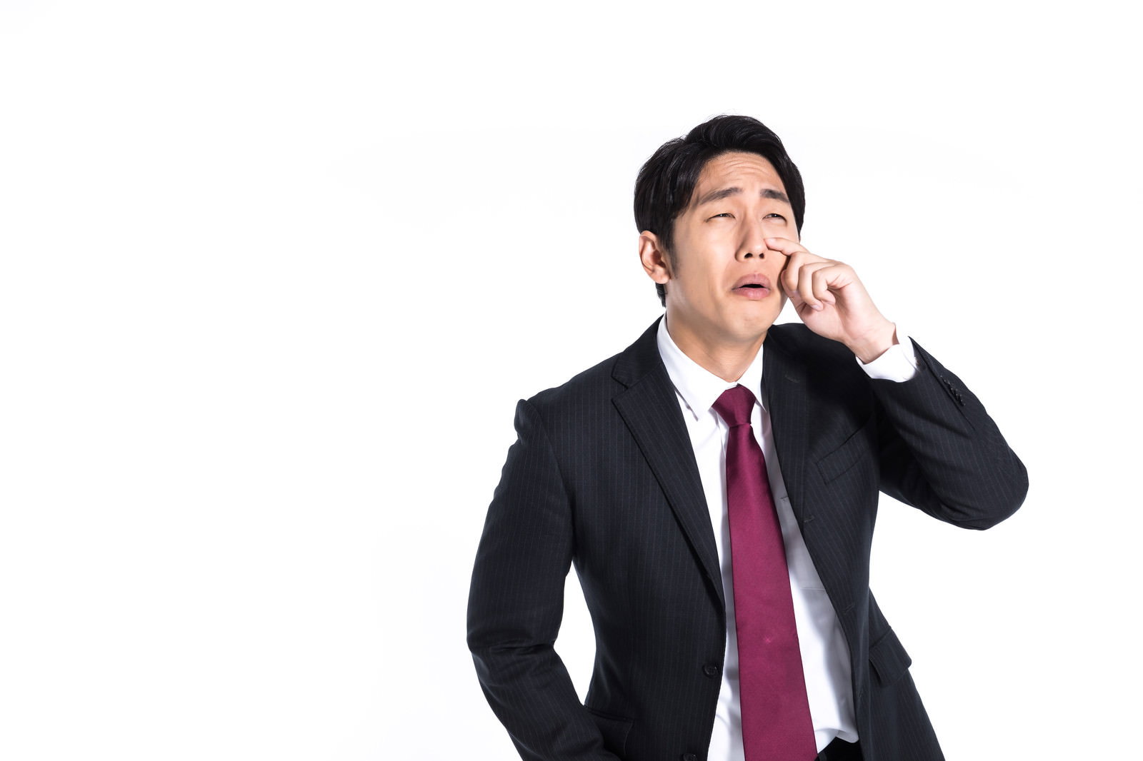 白背景で赤いネクタイのスーツ姿の営業マンが手で顔を覆いながら泣いている［モデル：大川竜弥］