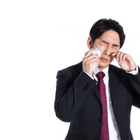 花粉症の季節、目の痒みで涙を流す会社員、ハンカチで涙を拭くの写真