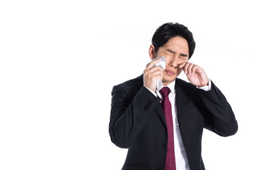 花粉症の季節、目の痒みで涙を流す会社員、ハンカチで涙を拭く