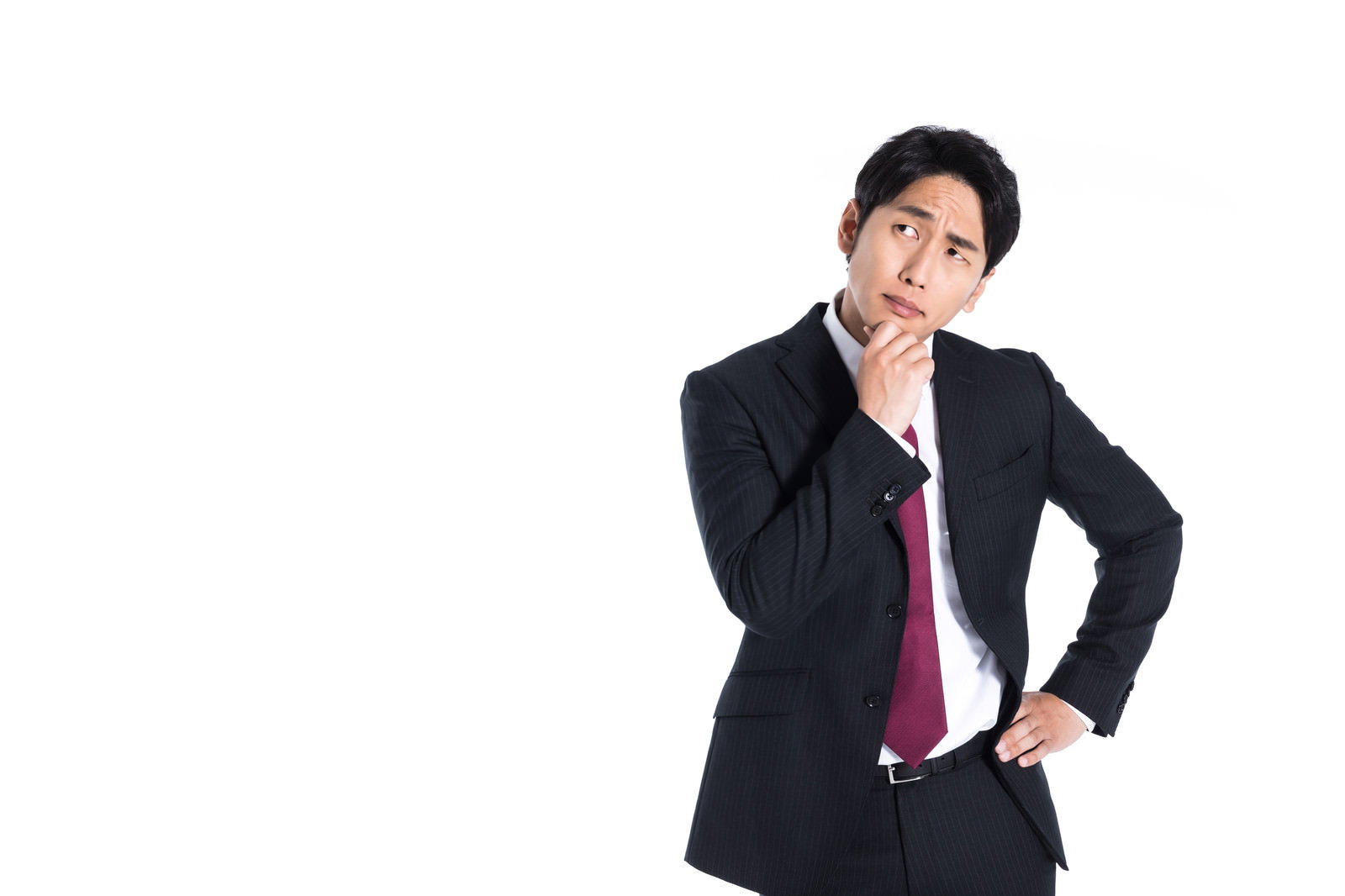黒いスーツを着た男性会社員が手を顎に当てて困惑した表情で考え込んでいる［モデル：大川竜弥］