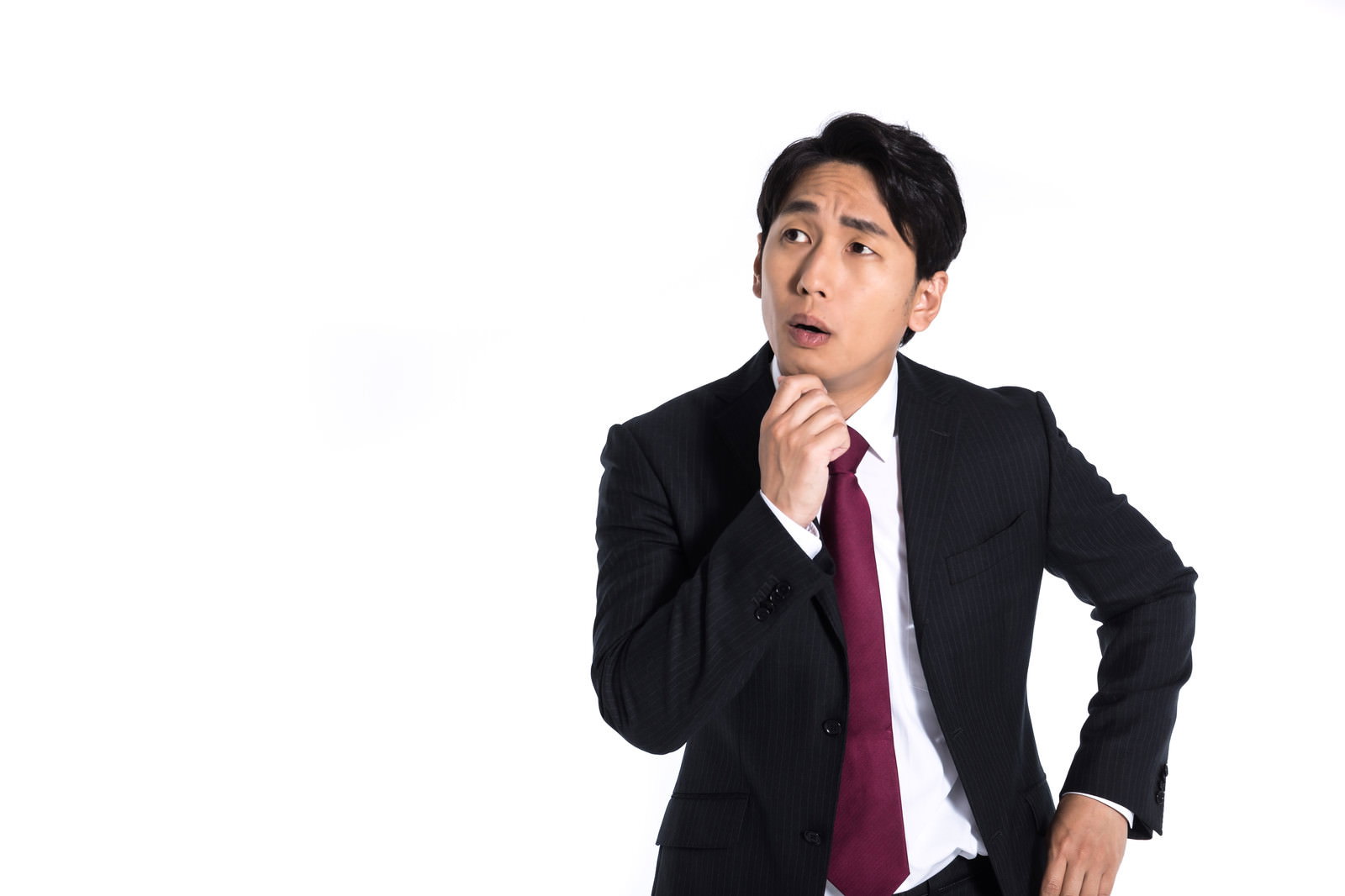 顎に手を当てて上を見上げながら考え込むスーツ姿の男性会社員［モデル：大川竜弥］