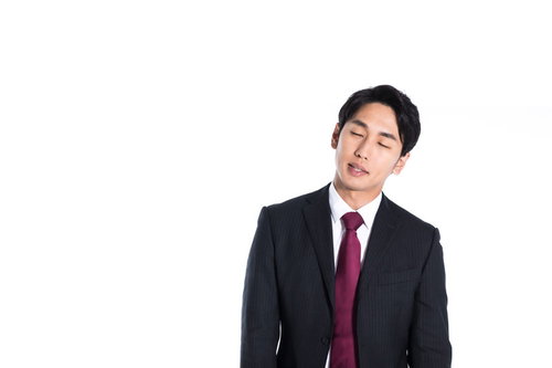 立ちながら寝落ち寸前のダークスーツ姿の営業マン