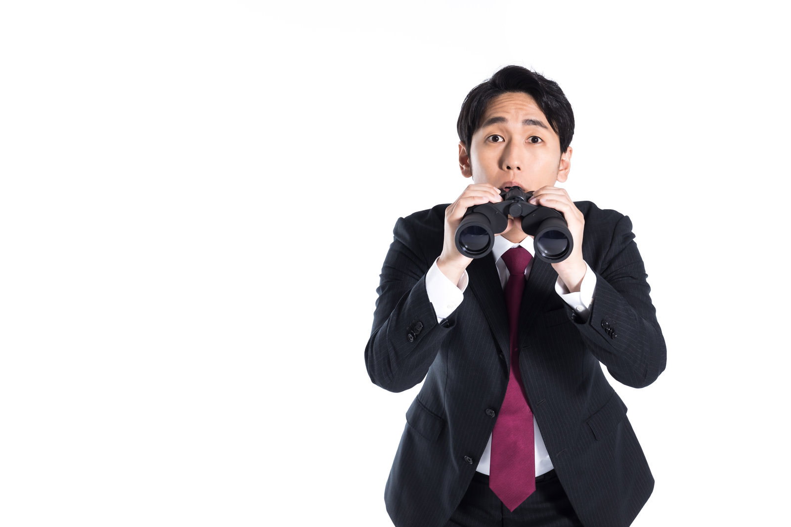 双眼鏡を両手で持って覗いている黒いスーツに赤いネクタイの男性［モデル：大川竜弥］
