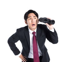 双眼鏡で探し物をするが見つからない会社員の写真