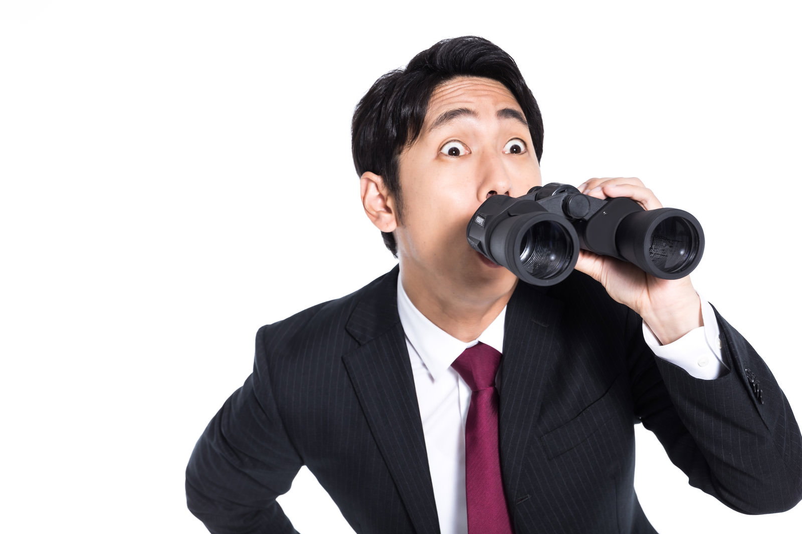 双眼鏡を両手で持って覗き込み、驚いた表情を見せるスーツ姿の会社員男性［モデル：大川竜弥］