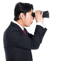 双眼鏡で競合他社をリサーチするスーツ姿のエージェントの写真