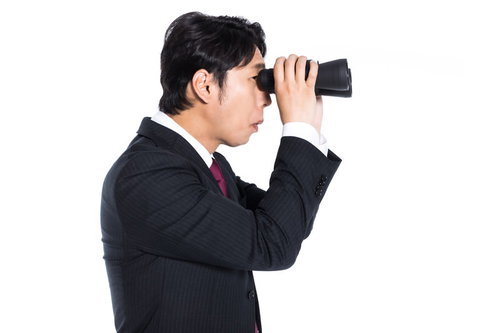 双眼鏡で競合他社をリサーチするスーツ姿のエージェント