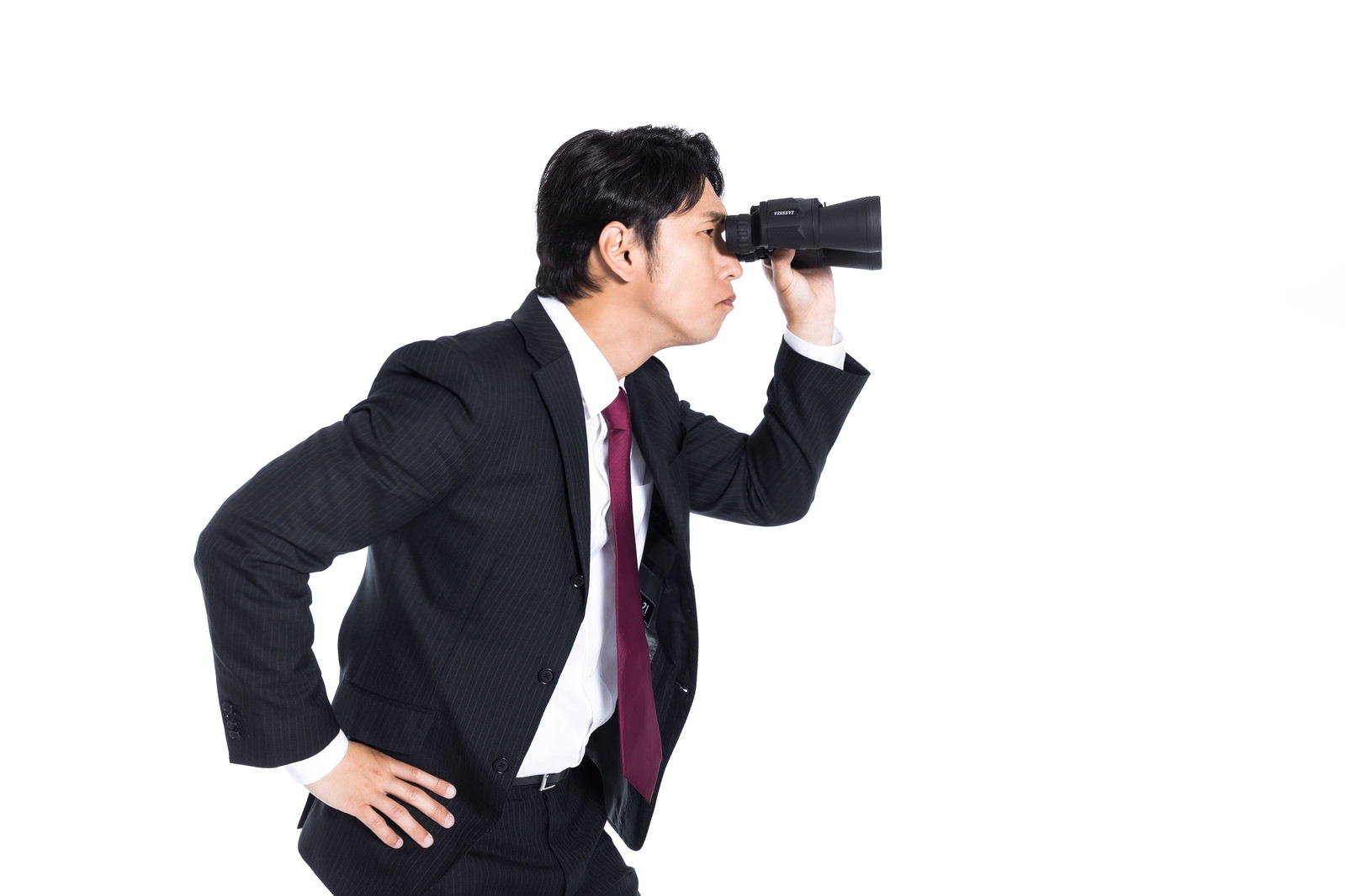 黒いスーツにえんじ色ネクタイの男性が黒い双眼鏡を両手で持ち、横向きで遠方を監視している