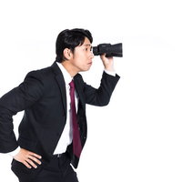 双眼鏡で遠くを監視するスーツ姿の男性の写真