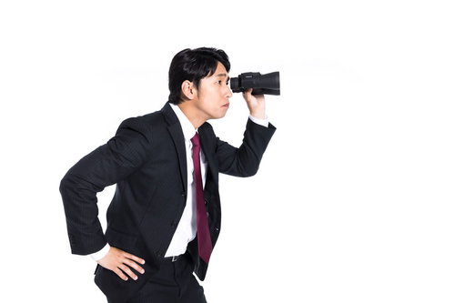 双眼鏡で遠くを監視するスーツ姿の男性