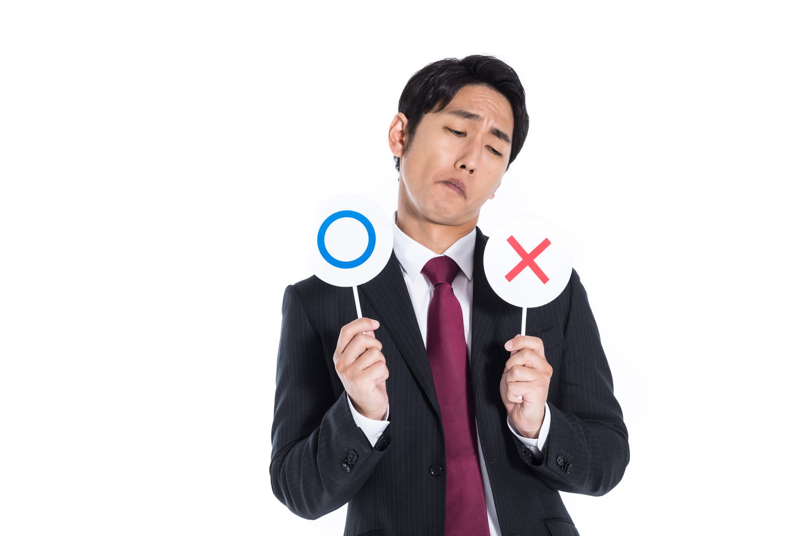 濃紺スーツの男性が左手に青い○、右手に赤い×の札を持ち、困った表情で判断に迷っている［モデル：大川竜弥］