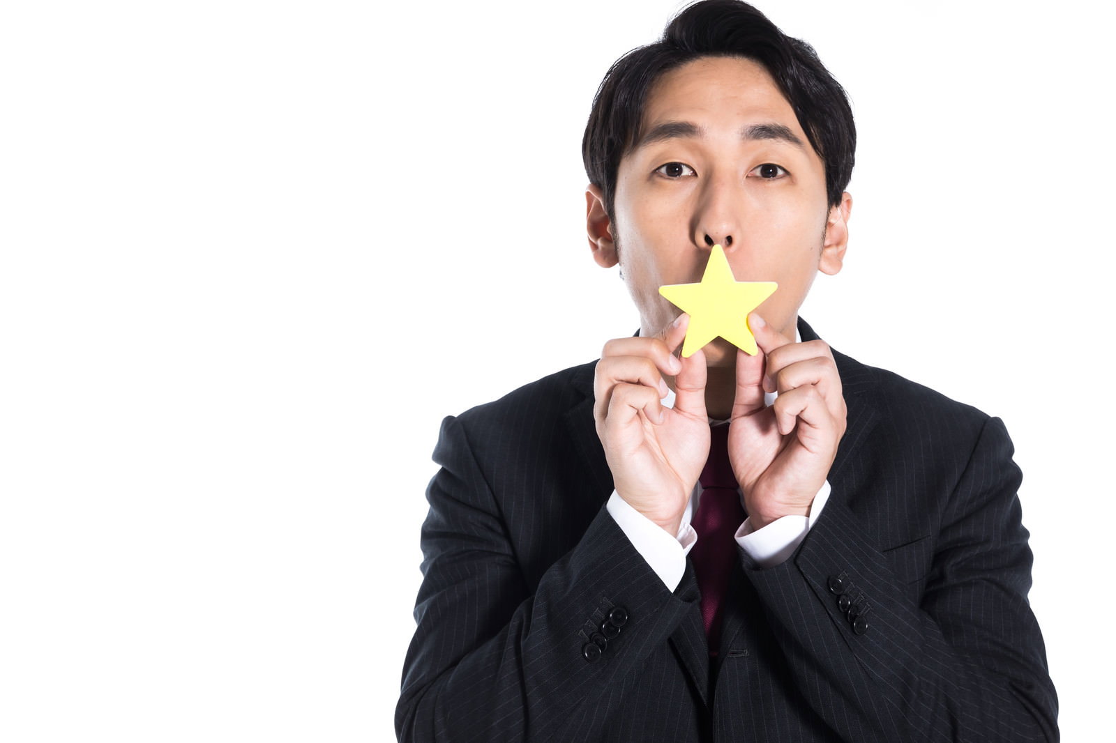黒いストライプスーツの男性が黄色い星を両手で口の高さに掲げている［モデル：大川竜弥］