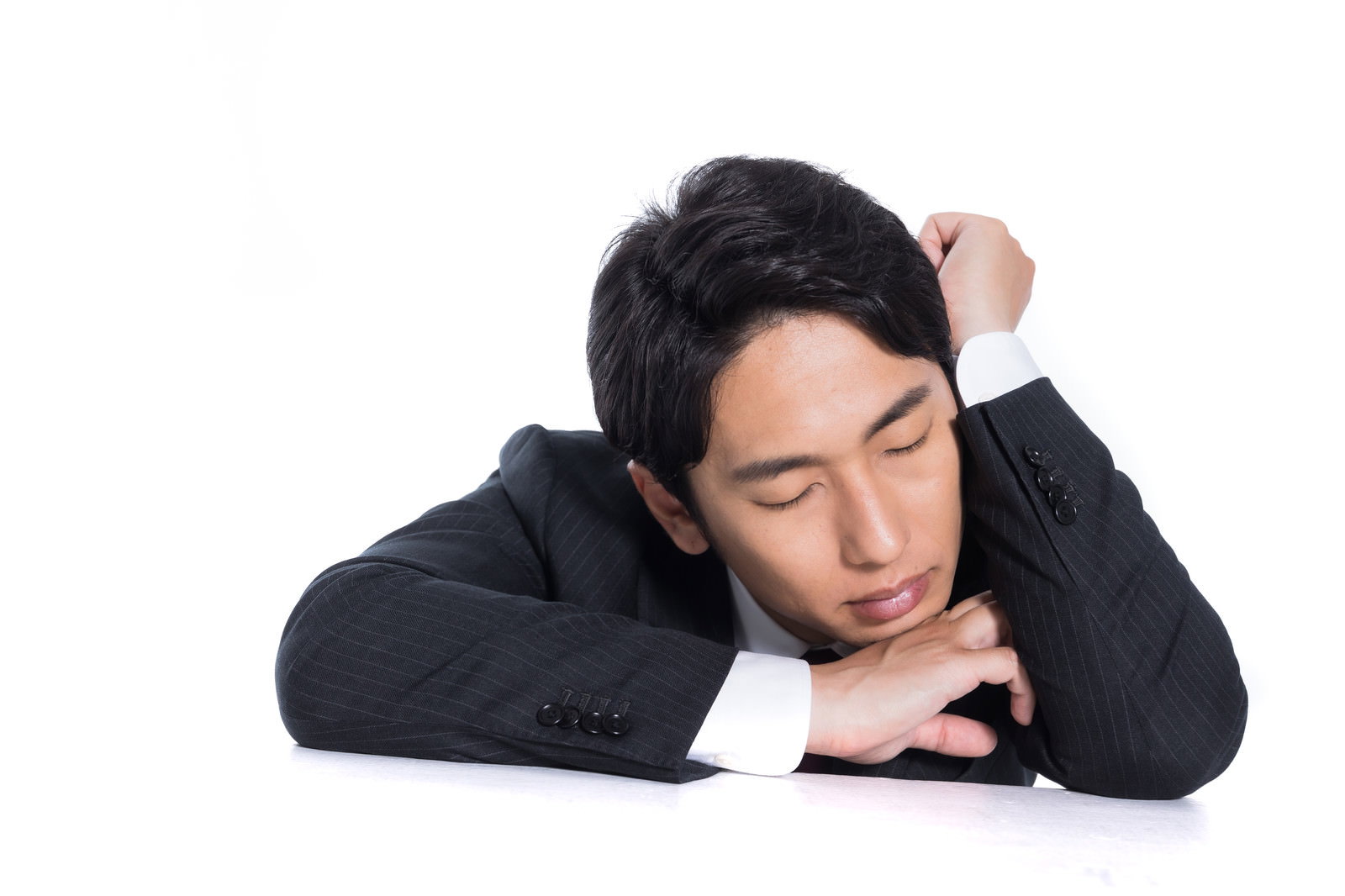 黒いスーツを着た男性会社員が机に肘をついて昼寝している［モデル：大川竜弥］