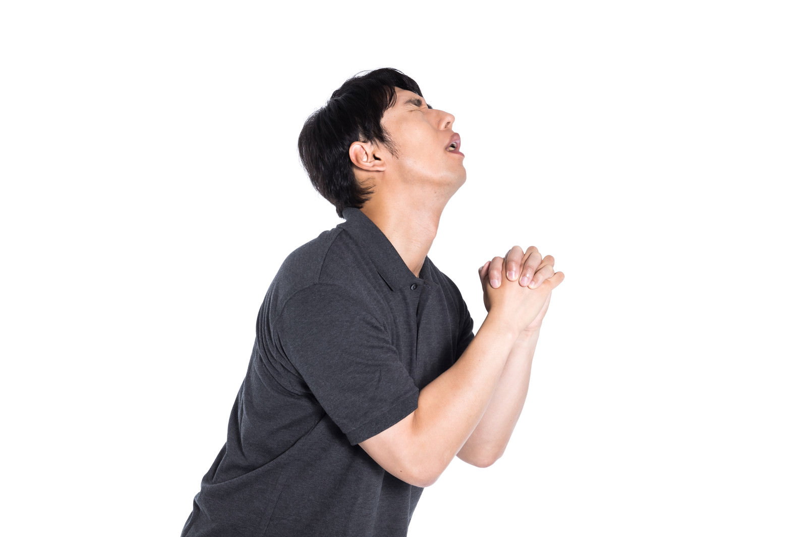 目を閉じて手を組み上を向いて祈りを捧げるグレーシャツの男性［モデル：大川竜弥］