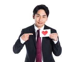 ハートマークを指して示すスーツ姿の男性の写真