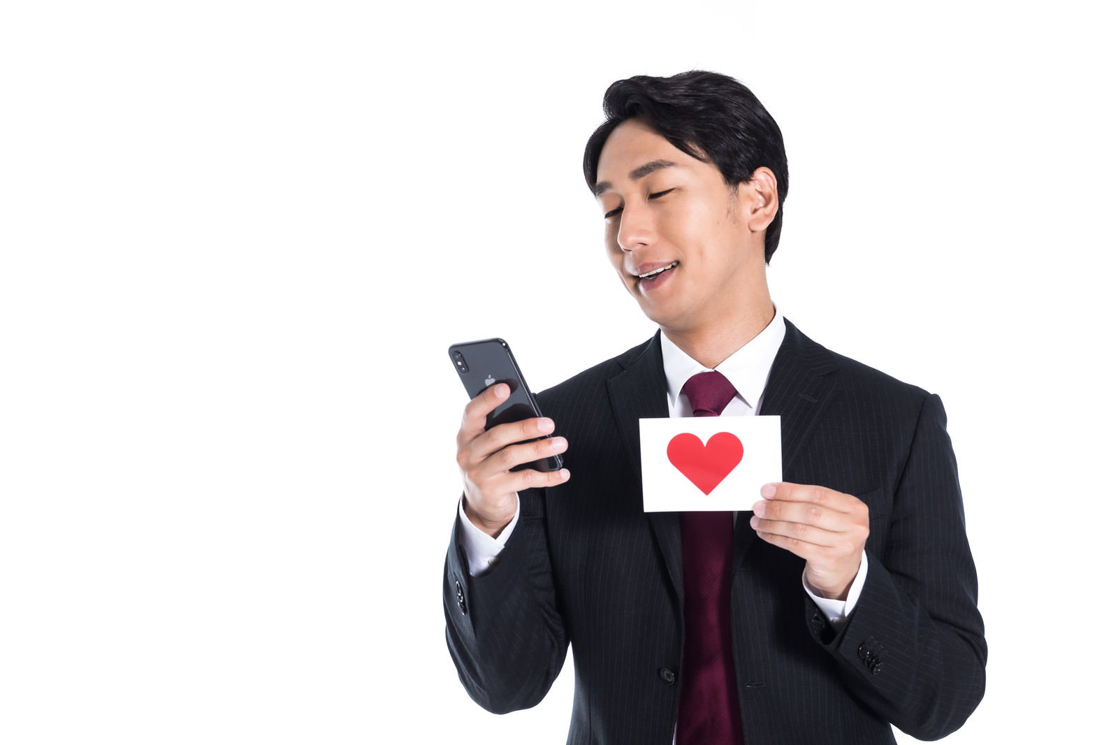 スマートフォンとハートカードを持つ黒いスーツ姿の男性［モデル：大川竜弥］