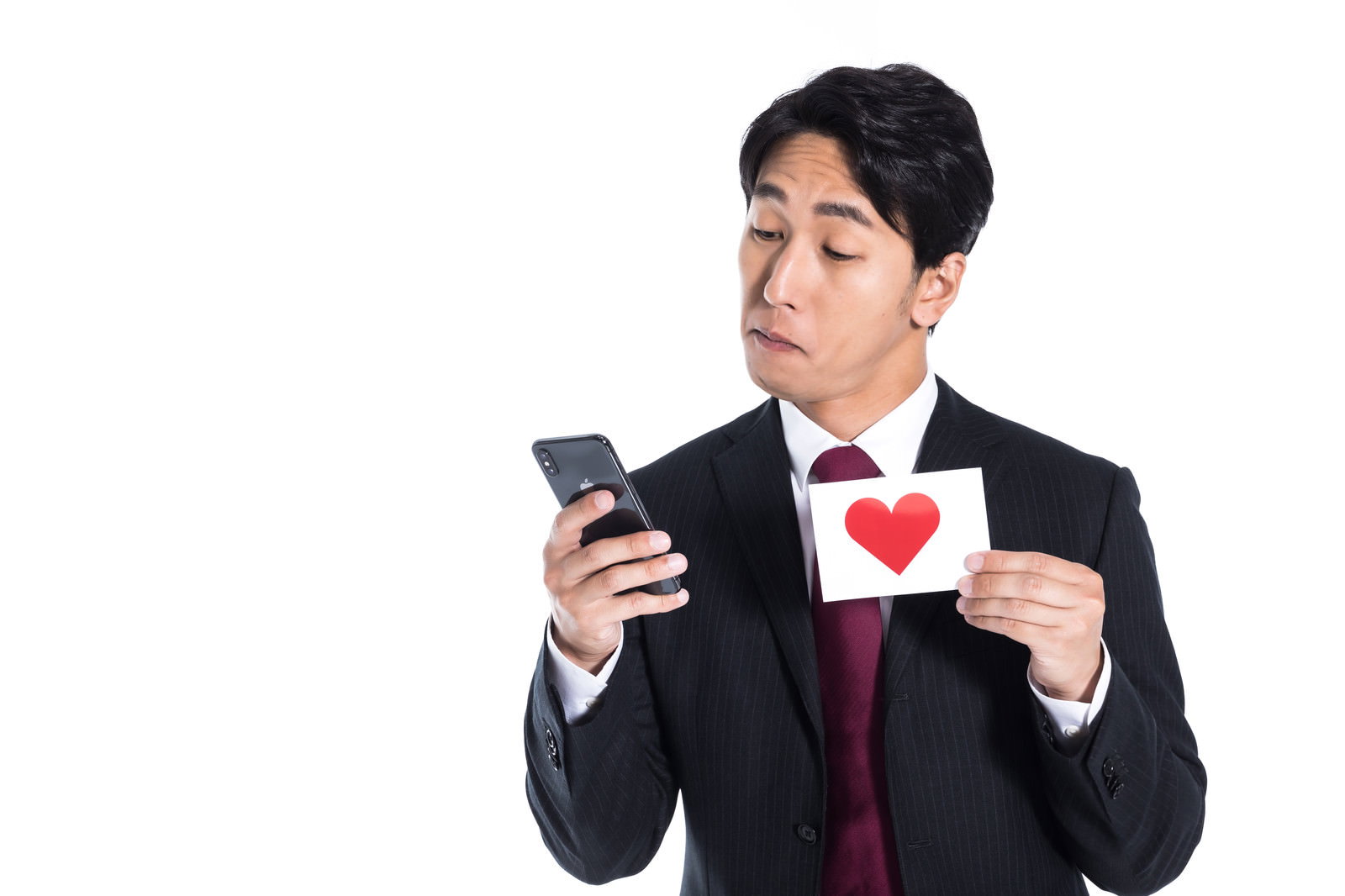 スマートフォンを持ちハート形のカードを見つめるスーツ姿の男性［モデル：大川竜弥］