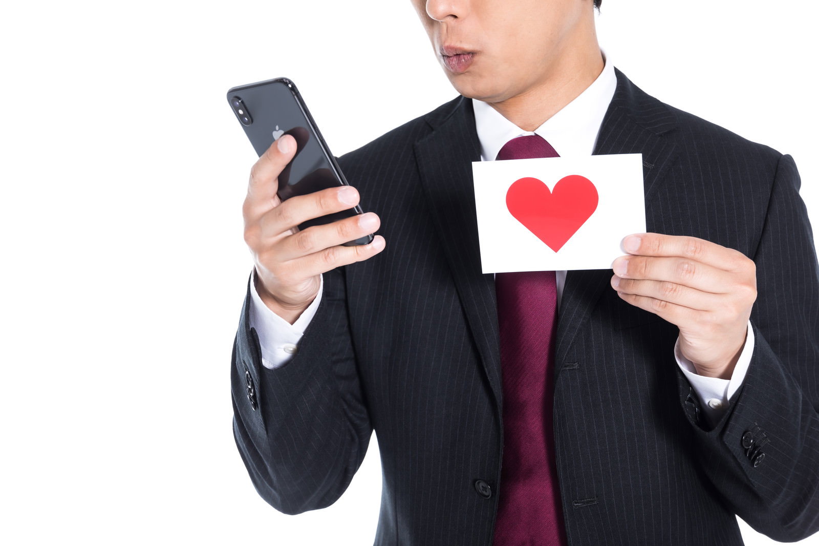 スマートフォンを見ながらハートマークのカードを持つスーツの男性［モデル：大川竜弥］