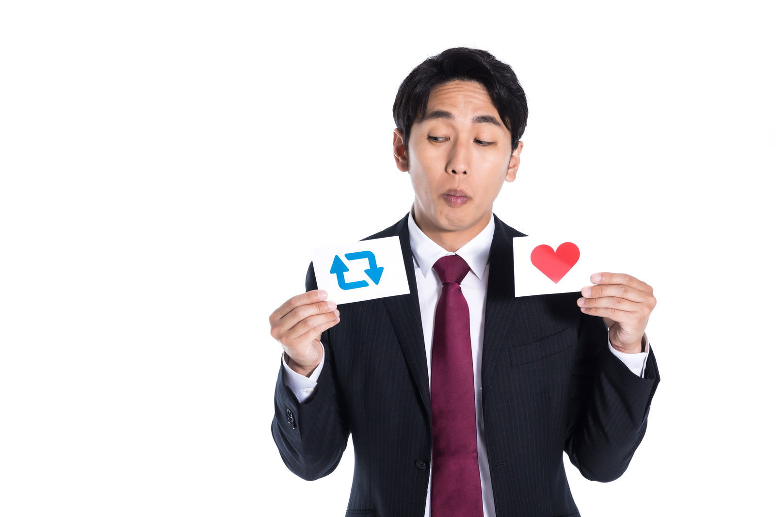 リツイートマークと赤いハートのカードを持って迷うスーツ姿の男性［モデル：大川竜弥］