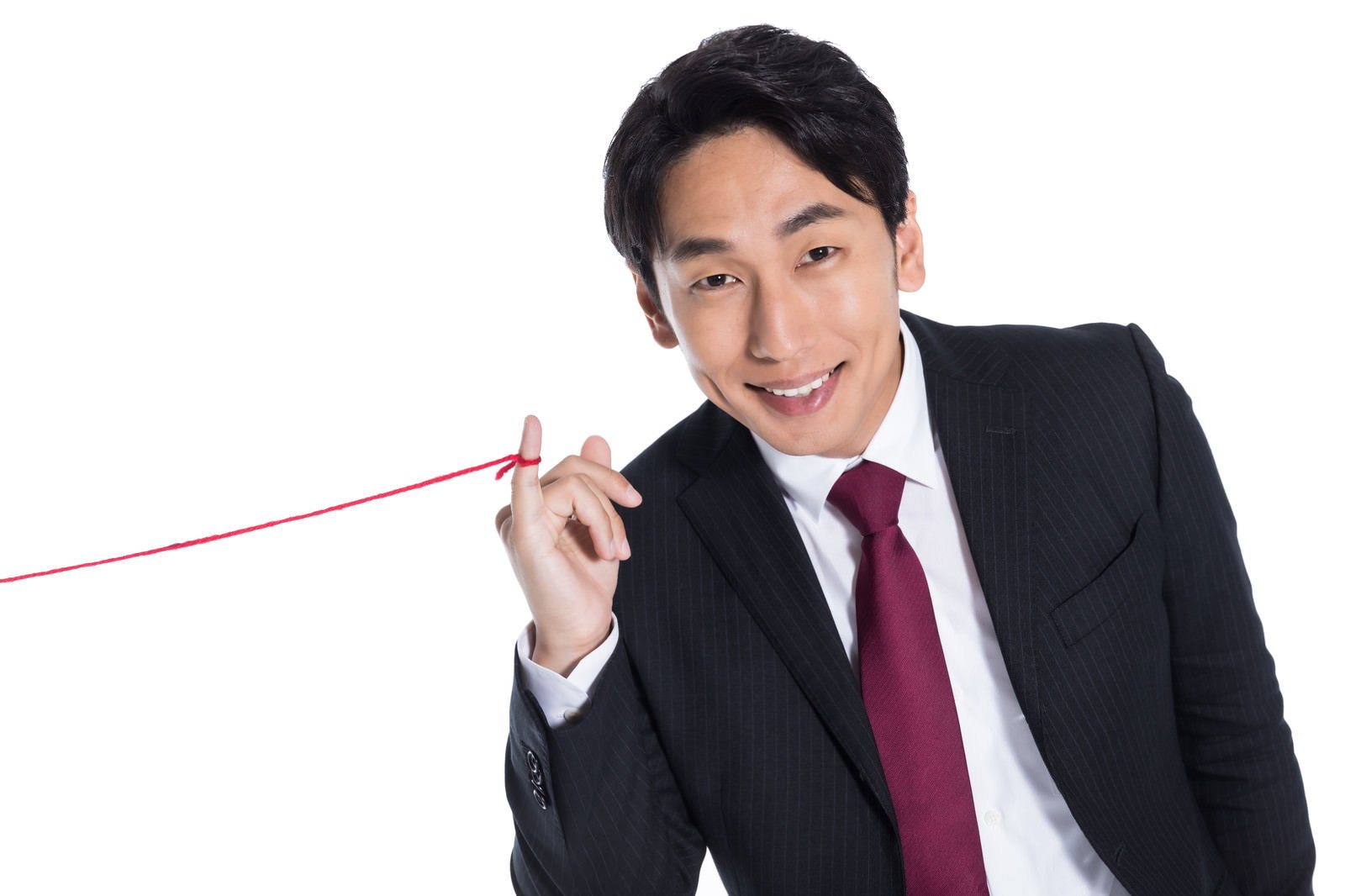 黒いスーツを着た男性が笑顔で赤い糸を手に持っている様子［モデル：大川竜弥］