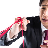 たくさんの運命の赤い糸に困惑するスーツ姿の男性の写真