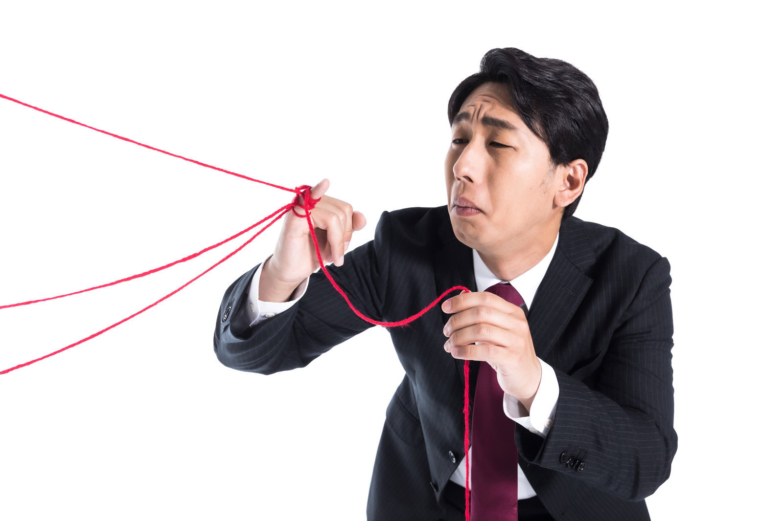 赤い糸に引っ張られて困惑した表情を見せるスーツ姿の男性［モデル：大川竜弥］