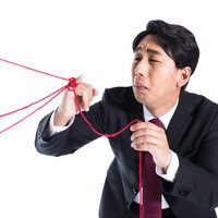 赤い糸に引っ張られて困惑するスーツ姿の男性の写真
