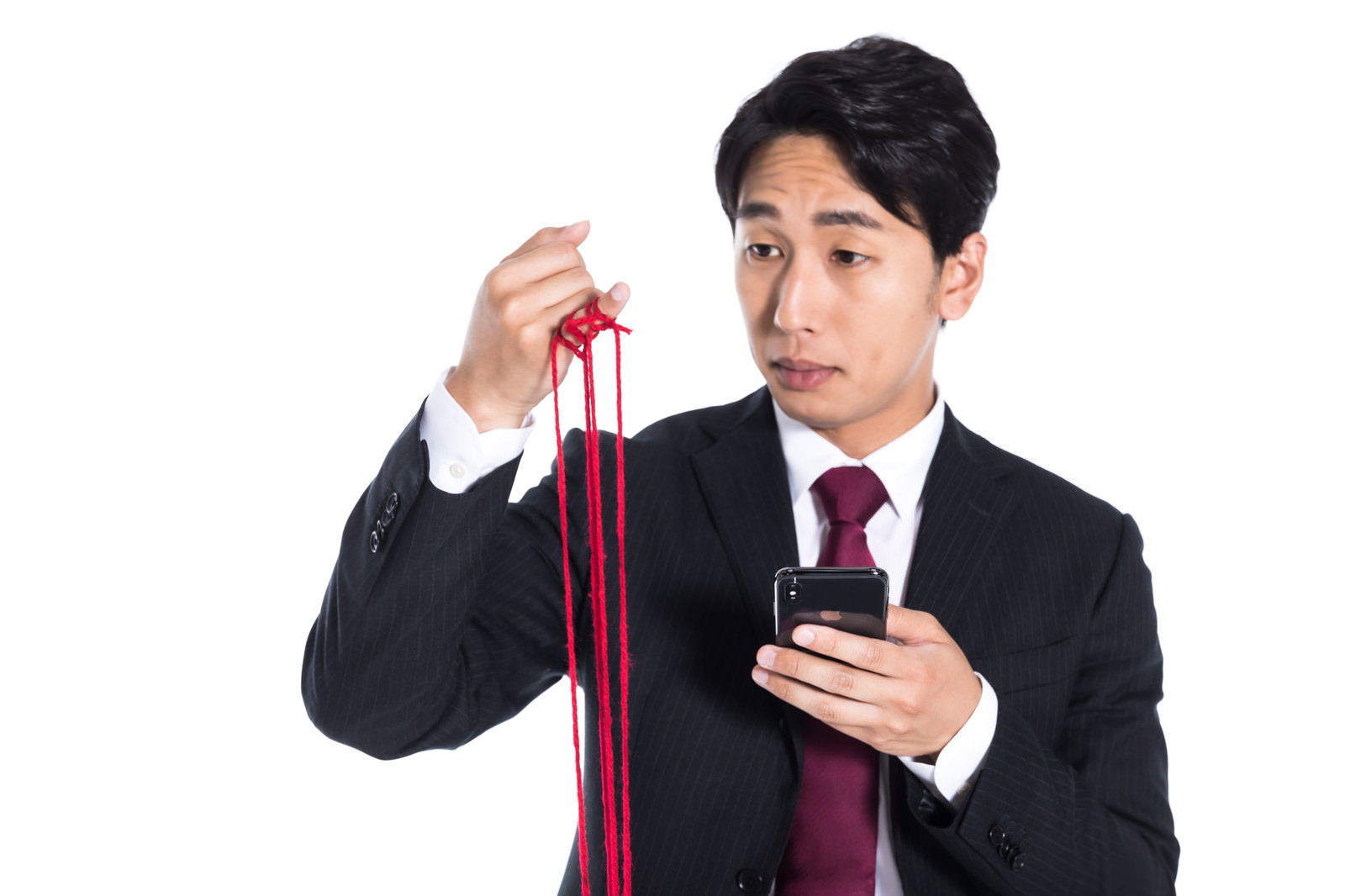 赤い糸を手に持ち見つめるスーツ姿の男性［モデル：大川竜弥］