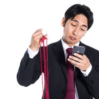 赤い糸を手にモテすぎて選びきれない男性がスマートフォンを操作の写真