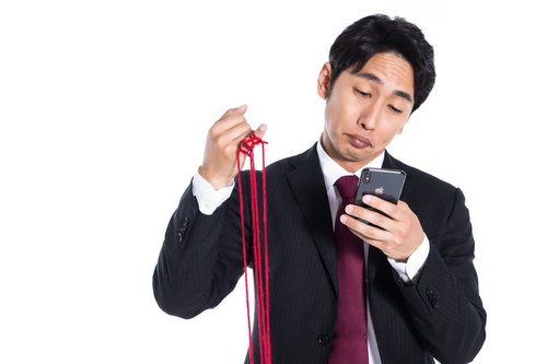 赤い糸を手にモテすぎて選びきれない男性がスマートフォンを操作