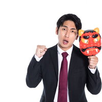 赤い鬼の面を手に怒りをあらわにするスーツ男性の写真