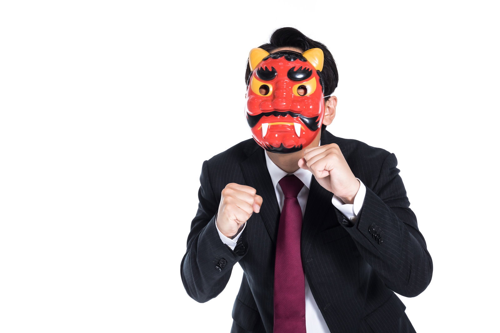 赤い鬼の面をかぶった黒スーツの男性がファイティングポーズをとっている［モデル：大川竜弥］